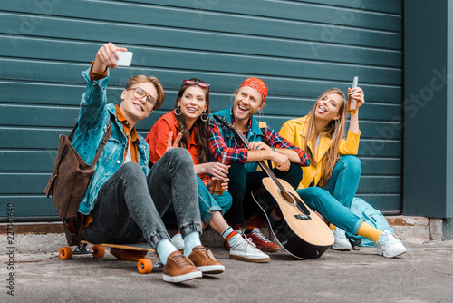 young friends with beer, skateboard and guitar taking selfie on smartphone
