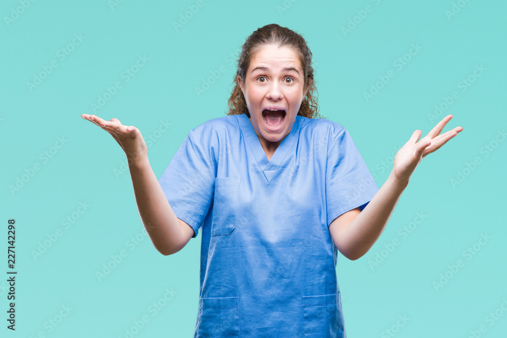 Young brunette doctor girl wearing nurse or surgeon uniform over isolated background celebrating crazy and amazed for success with arms raised and open eyes screaming excited. Winner concept