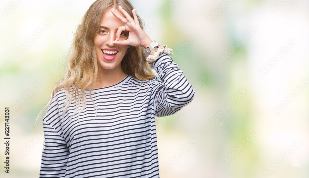 Beautiful young blonde woman wearing stripes sweater over isolated background doing ok gesture with hand smiling, eye looking through fingers with happy face. Beautiful young blonde woman wearing stripes sweater over isolated background doing ok gesture with hand smiling, eye looking through fingers with happy face.