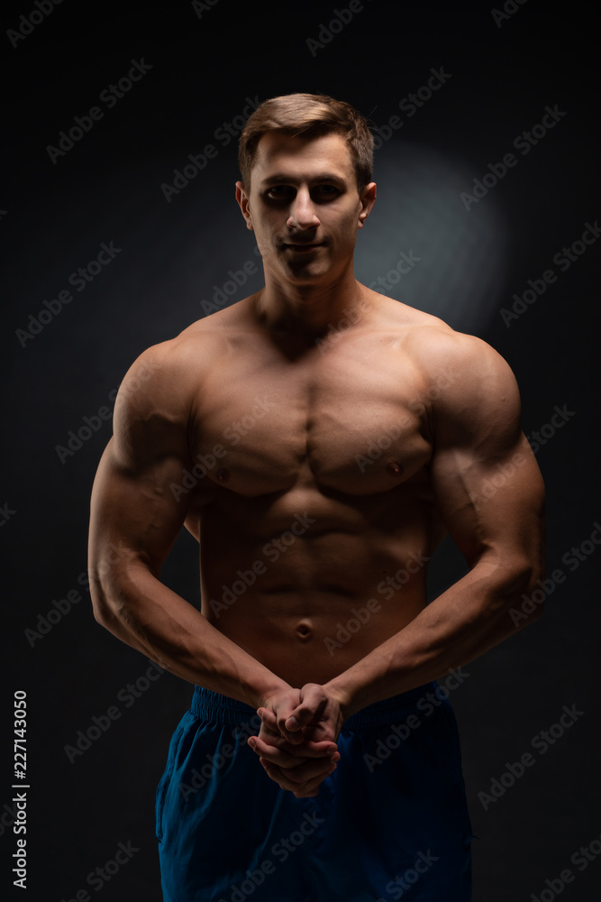 young, Strong bodybuilder with six packs. Bodybuilder flexes muscles against dark background young, Strong bodybuilder with six packs. Bodybuilder flexes muscles against dark background