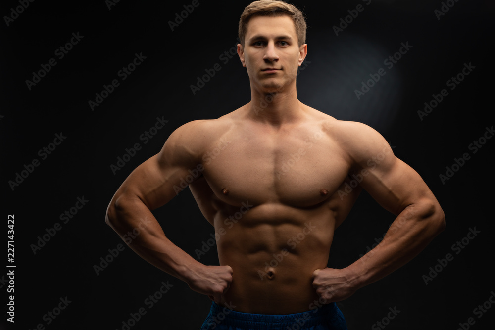 young, Strong bodybuilder with six packs. Bodybuilder flexes muscles against dark background