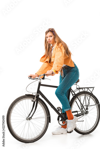 hipster girl sitting on bicycle and looking at camera isolated on white
