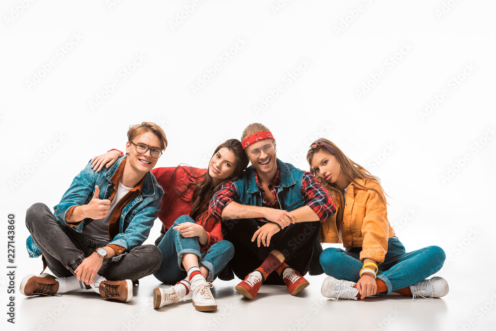 Obraz premium young male hipster man in denim jacket showing thumb up while his friends sitting near isolated on white