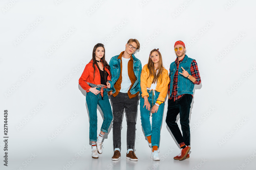Fototapeta premium young stylish hipsters posing together while man showing rock and roll gesture on grey
