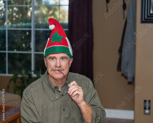 Older male thinks with glasses wearing holiday elf hat