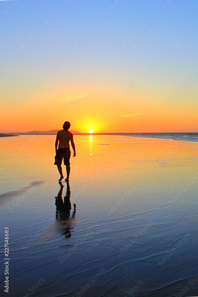 Young man walking on the beach at sunset time
