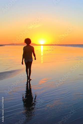 Woman walks on the beach while the sun sets in Jericoacoara - vertical