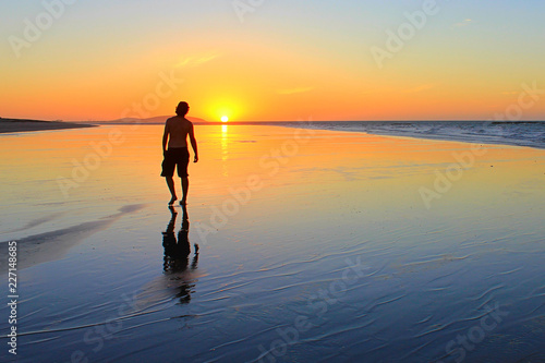 Young man walking on the beach at sunset time photo