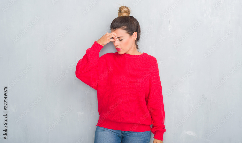 Young adult woman over grey grunge wall wearing winter outfit tired rubbing nose and eyes feeling fatigue and headache. Stress and frustration concept. Young adult woman over grey grunge wall wearing winter outfit tired rubbing nose and eyes feeling fatigue and headache. Stress and frustration concept.