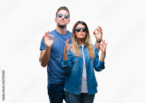 Young couple in love wearing sunglasses over isolated background relax and smiling with eyes closed doing meditation gesture with fingers. Yoga concept.