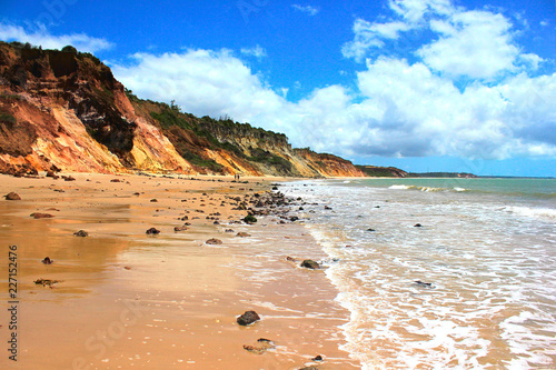 Sunny day at Praia do Amor Beach: multicolored cliffs, rocks, wet sand, sea and blue sky