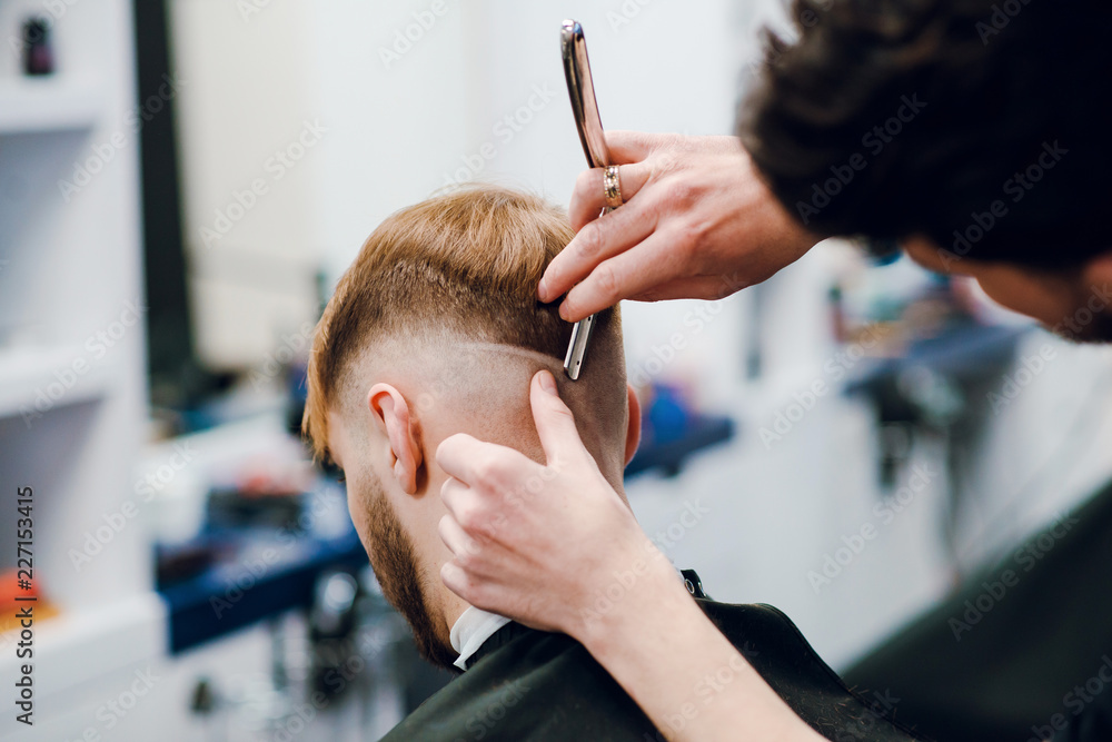 Close up male hairdresser cuts mans hair with scissors in a barber shop. Back view Close up male hairdresser cuts mans hair with scissors in a barber shop. Back view