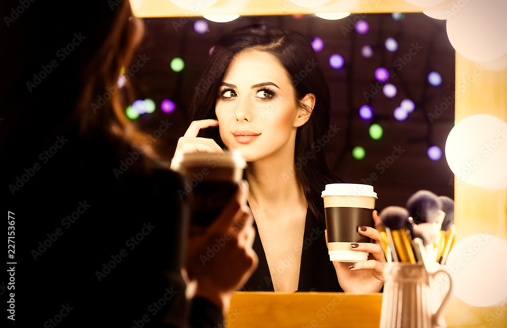 portrait of young beautiful woman with cup of coffee looking in the mirror