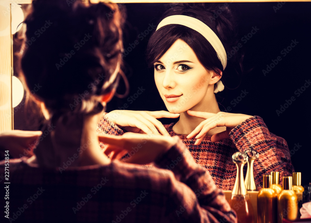 Naklejka premium Portrait of a beautiful woman near a mirror applying cosmetics