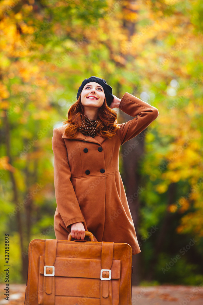 Redhead girl with suitcase in a park. Autumn season Redhead girl with suitcase in a park. Autumn season