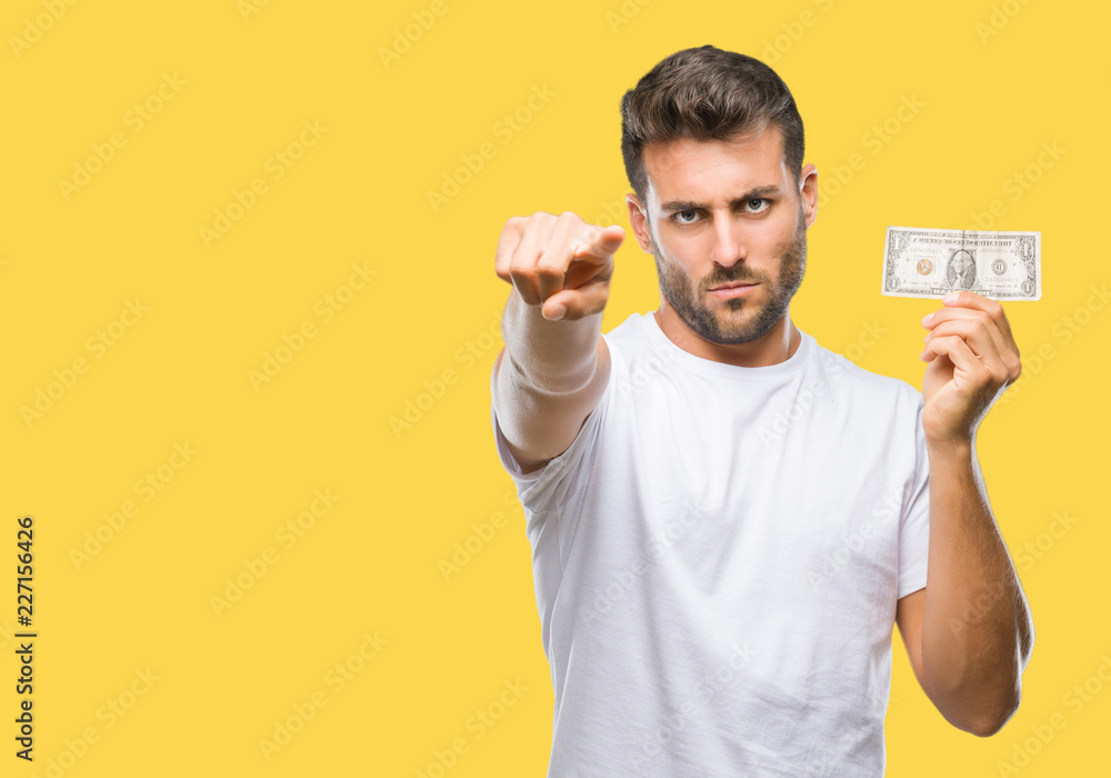 Young handsome man holding dollars over isolated background pointing with finger to the camera and to you, hand sign, positive and confident gesture from the front Young handsome man holding dollars over isolated background pointing with finger to the camera and to you, hand sign, positive and confident gesture from the front