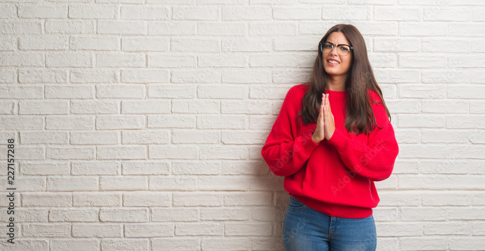 Young brunette woman standing over white brick wall begging and praying with hands together with hope expression on face very emotional and worried. Asking for forgiveness. Religion concept. Young brunette woman standing over white brick wall begging and praying with hands together with hope expression on face very emotional and worried. Asking for forgiveness. Religion concept.