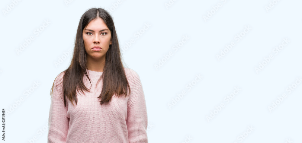 Fototapeta premium Young beautiful hispanic woman wearing a sweater with serious expression on face. Simple and natural looking at the camera.