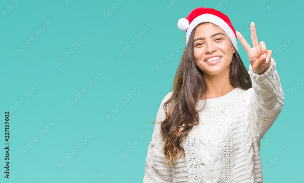 Young arab woman wearing christmas hat over isolated background smiling with happy face winking at the camera doing victory sign. Number two. Young arab woman wearing christmas hat over isolated background smiling with happy face winking at the camera doing victory sign. Number two.