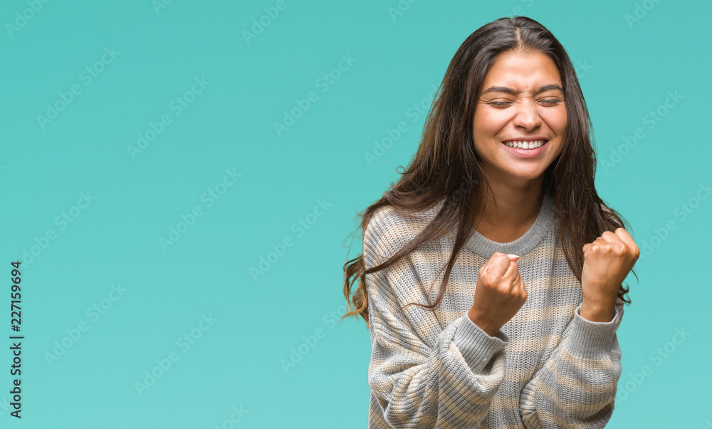 Young beautiful arab woman wearing winter sweater over isolated background very happy and excited doing winner gesture with arms raised, smiling and screaming for success. Celebration concept. Young beautiful arab woman wearing winter sweater over isolated background very happy and excited doing winner gesture with arms raised, smiling and screaming for success. Celebration concept.