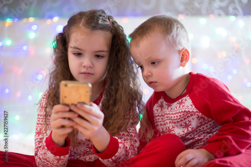 children in Christmas pajamas playing smartphone
