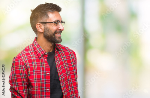 Adult hispanic man wearing glasses over isolated background looking away to side with smile on face, natural expression. Laughing confident.
