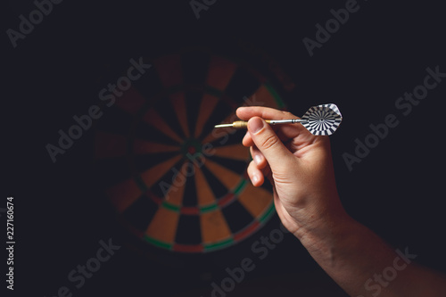 Hand holding a dart aiming at the target - business targeting, aiming, focus concept.