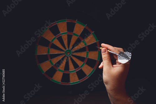 Hand holding a dart aiming at the target - business targeting, aiming, focus concept.
