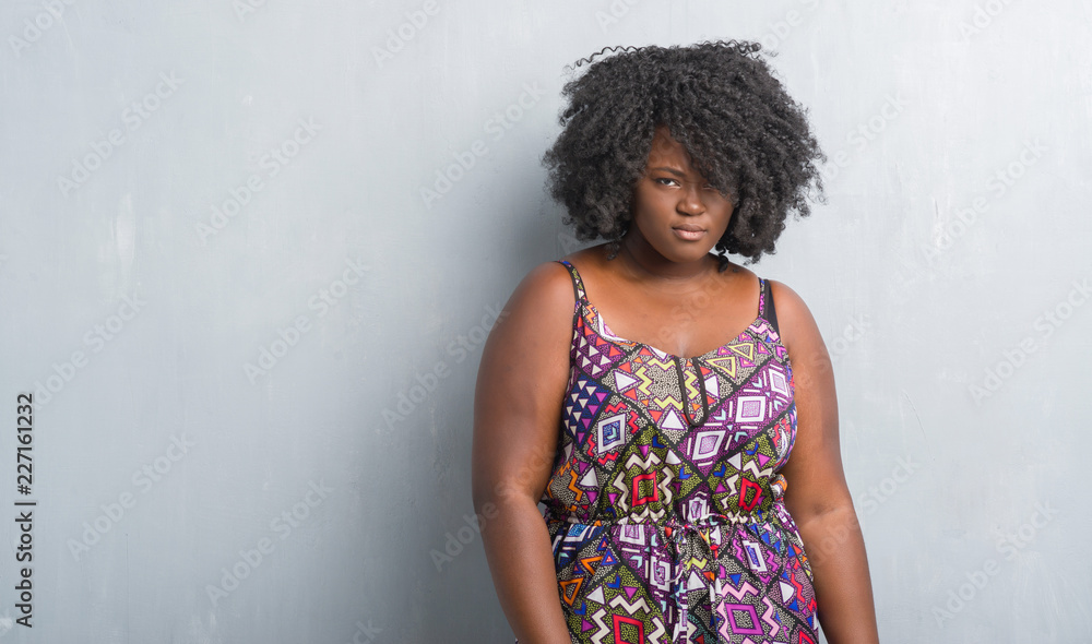 Young african american woman over grey grunge wall wearing colorful dress skeptic and nervous, frowning upset because of problem. Negative person. Young african american woman over grey grunge wall wearing colorful dress skeptic and nervous, frowning upset because of problem. Negative person.