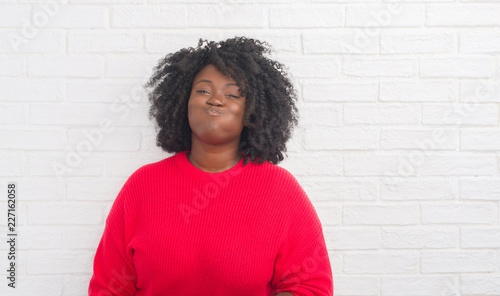 Young african american plus size woman over white brick wall puffing cheeks with funny face. Mouth inflated with air, crazy expression.
