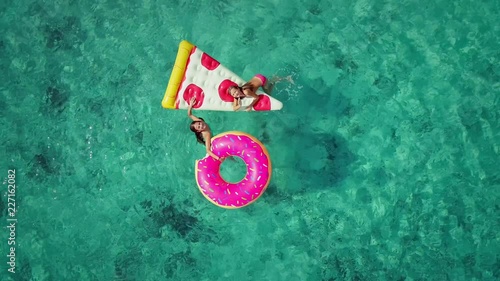 Close up aerial view of two young girls swimming and playing in sea with inflatable pizza and donut matresses. photo