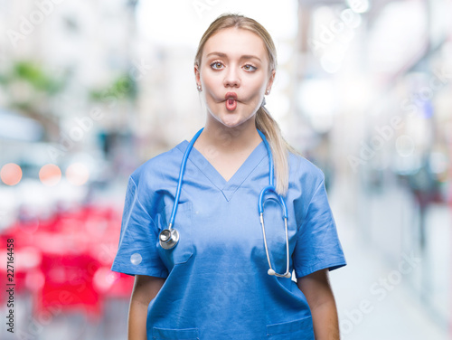 Young blonde surgeon doctor woman over isolated background making fish face with lips, crazy and comical gesture. Funny expression.