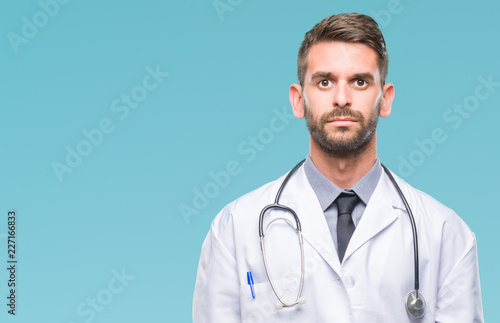 Young handsome doctor man over isolated background with serious expression on face. Simple and natural looking at the camera.