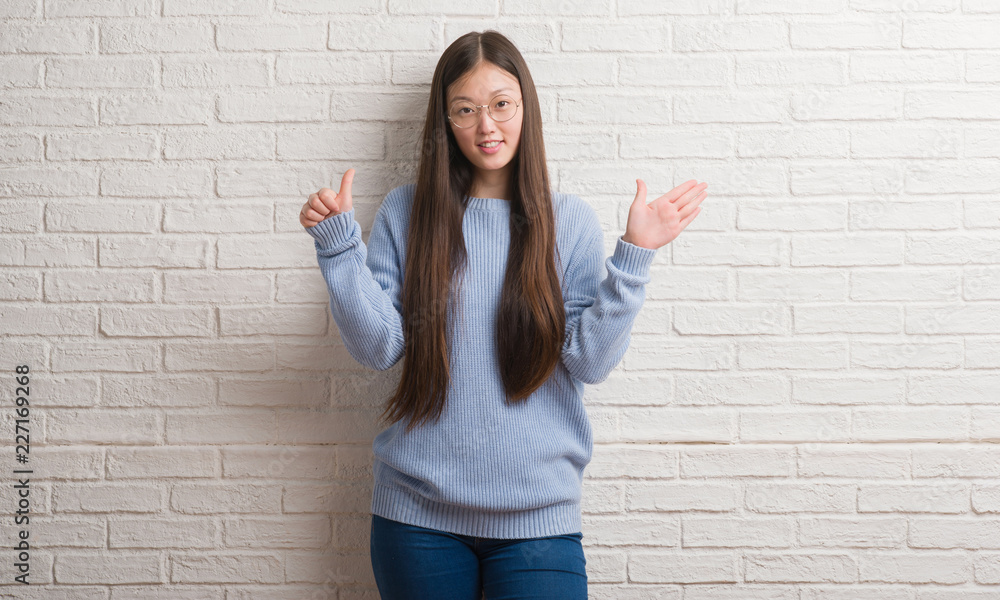 Young Chinise woman over white brick wall showing and pointing up with fingers number six while smiling confident and happy. Young Chinise woman over white brick wall showing and pointing up with fingers number six while smiling confident and happy.