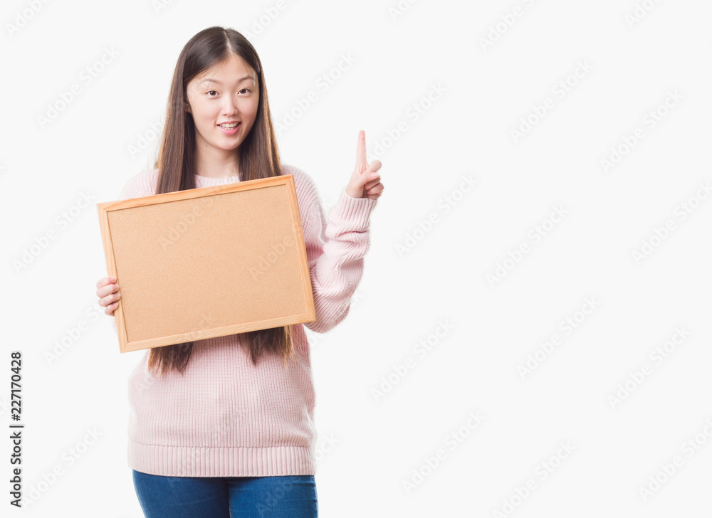 Young Chinese woman over isolated background holding corkboard surprised with an idea or question pointing finger with happy face, number one Young Chinese woman over isolated background holding corkboard surprised with an idea or question pointing finger with happy face, number one