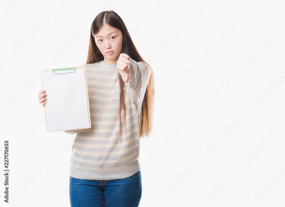 Young Chinese woman over isolated background holding clipboard with angry face, negative sign showing dislike with thumbs down, rejection concept Young Chinese woman over isolated background holding clipboard with angry face, negative sign showing dislike with thumbs down, rejection concept