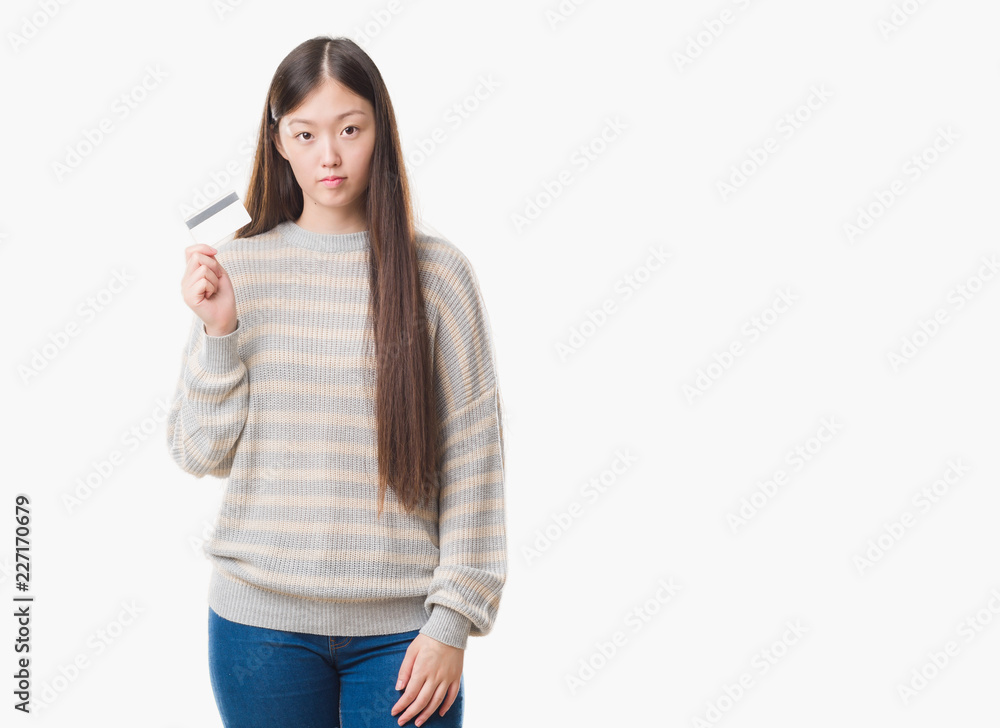 Young Chinese woman over isolated background holding credit card with a confident expression on smart face thinking serious Young Chinese woman over isolated background holding credit card with a confident expression on smart face thinking serious