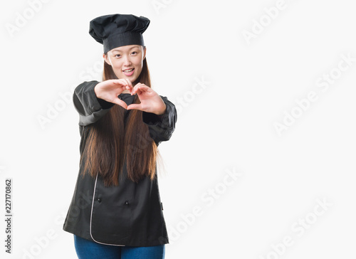 Young Chinese woman over isolated background wearing chef uniform smiling in love showing heart symbol and shape with hands. Romantic concept.