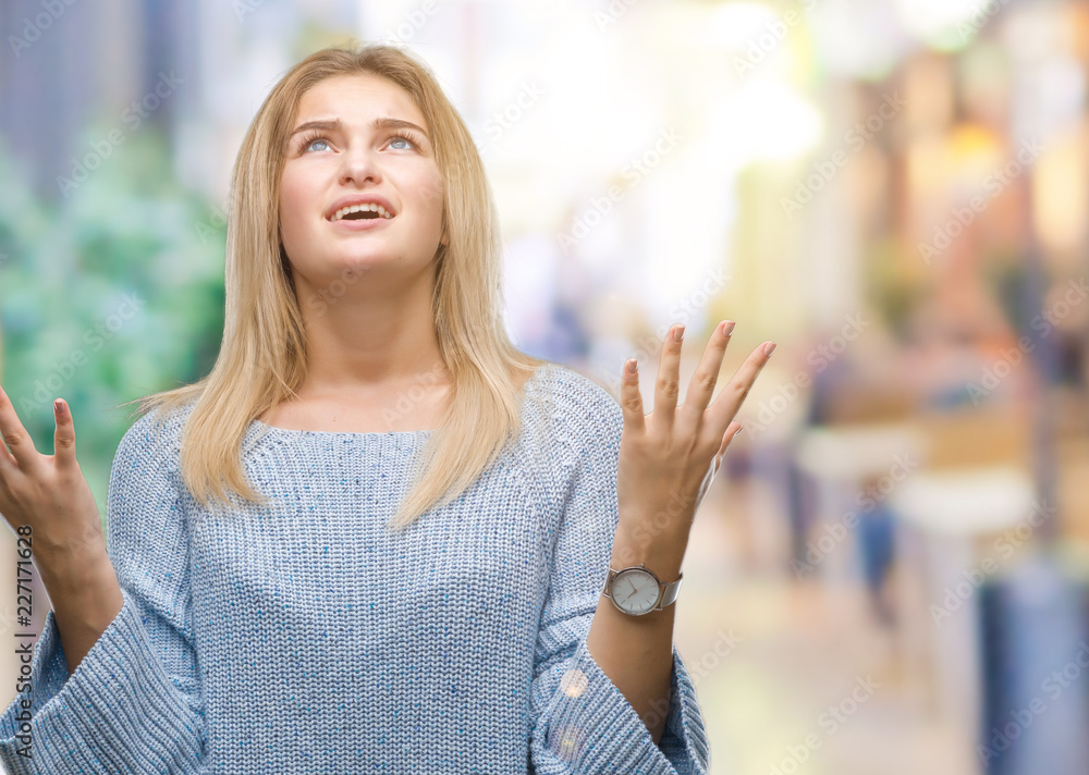 Young caucasian woman wearing winter sweater over isolated background crazy and mad shouting and yelling with aggressive expression and arms raised. Frustration concept. Young caucasian woman wearing winter sweater over isolated background crazy and mad shouting and yelling with aggressive expression and arms raised. Frustration concept.