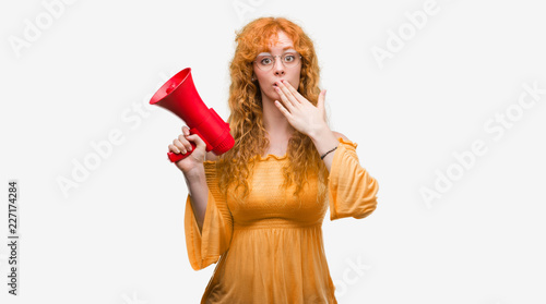 Young redhead woman holding megaphone cover mouth with hand shocked with shame for mistake, expression of fear, scared in silence, secret concept