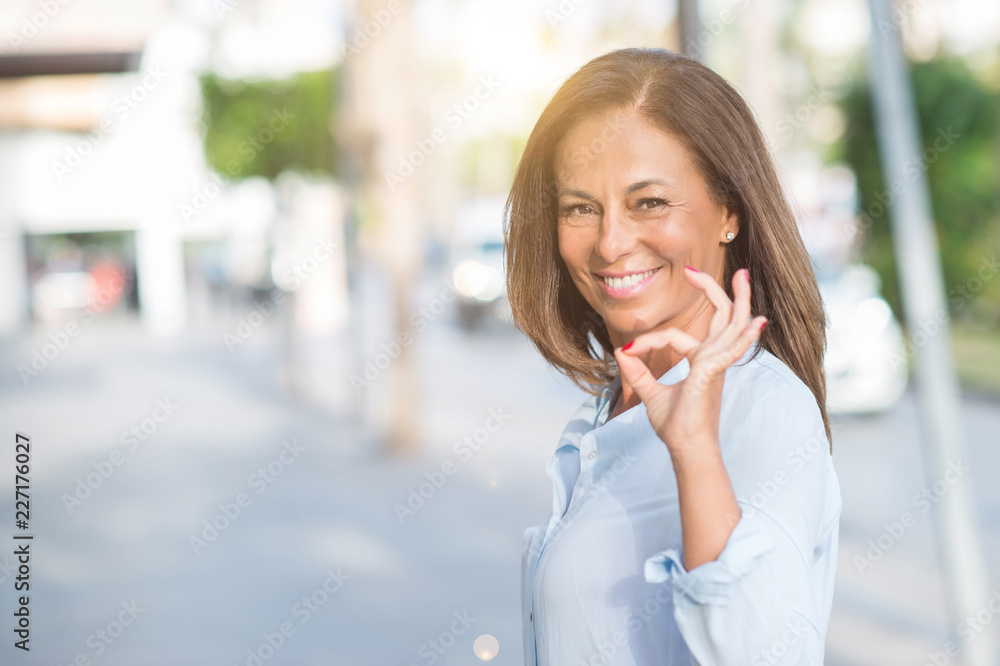 Beautiful middle age hispanic woman at the city street on a sunny day doing ok sign with fingers, excellent symbol Beautiful middle age hispanic woman at the city street on a sunny day doing ok sign with fingers, excellent symbol