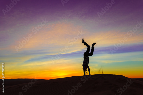 Silhouette of woman doing hand stand on sand dune during the sunset