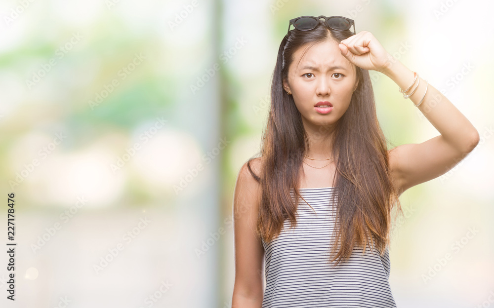 Young asian woman wearing sunglasses over isolated background angry and mad raising fist frustrated and furious while shouting with anger. Rage and aggressive concept.