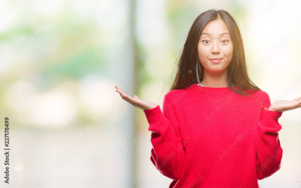 Young asian woman wearing winter sweater over isolated background clueless and confused expression with arms and hands raised. Doubt concept. Young asian woman wearing winter sweater over isolated background clueless and confused expression with arms and hands raised. Doubt concept.