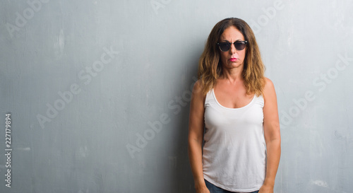 Middle age hispanic woman over grey wall wearing sunglasses depressed and worry for distress, crying angry and afraid. Sad expression.