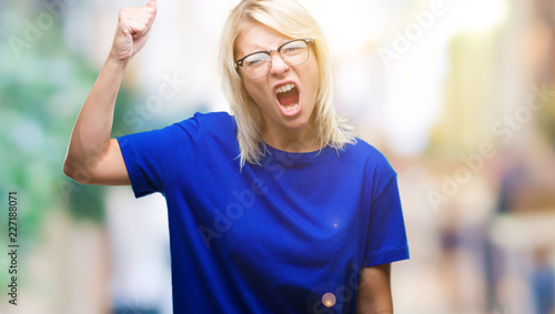 Young beautiful blonde woman wearing glasses over isolated background angry and mad raising fist frustrated and furious while shouting with anger. Rage and aggressive concept.