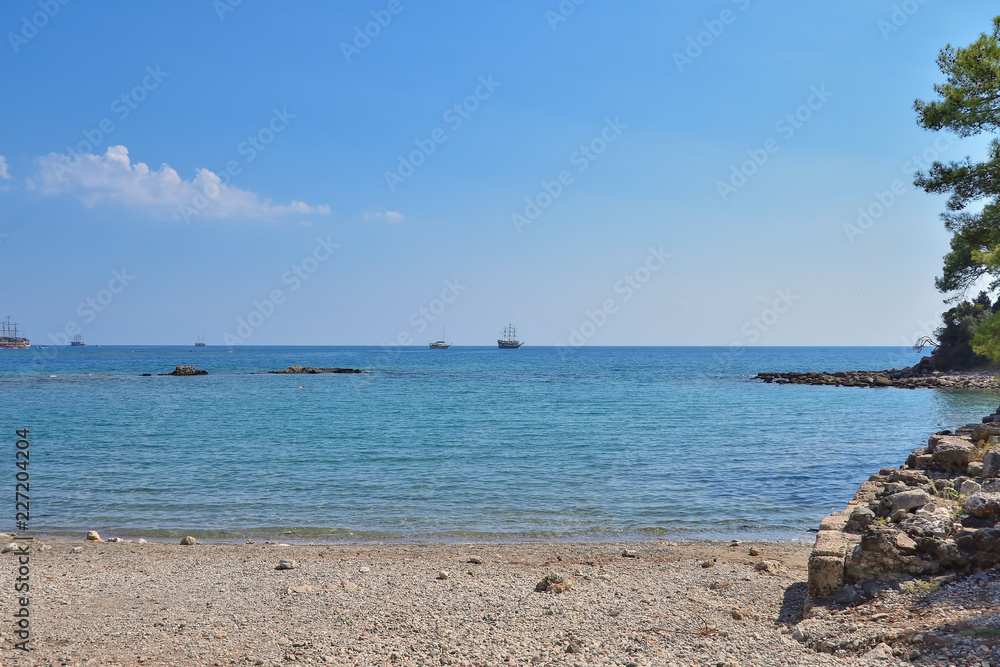 quiet bay in the area of the historic ruins of the city of Phaselis, beautiful sea, green vegetation, ships and yachts in anchorage, against the backdrop of mountains and clouds