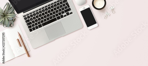 modern header / hero image or banner with laptop computer, smartphone, air plant, open notebook and feminine accessories on a bright blush background, home office scene, flat lay / top view