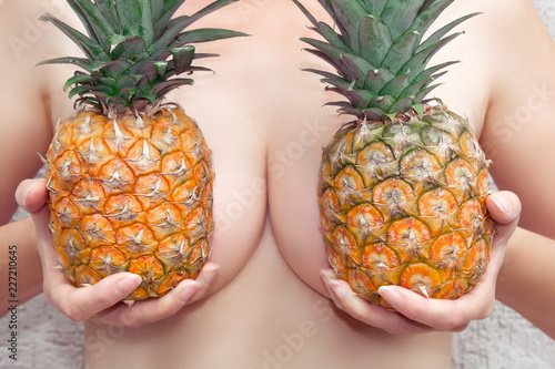 A young woman holds pineapples at her breasts. Bra from pineapples. Close-up.