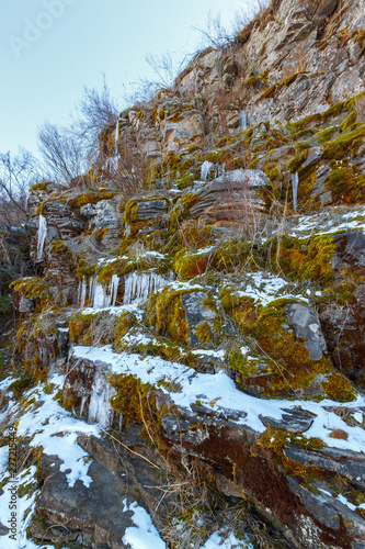 The cascade slope of the rock with mosses and icicles